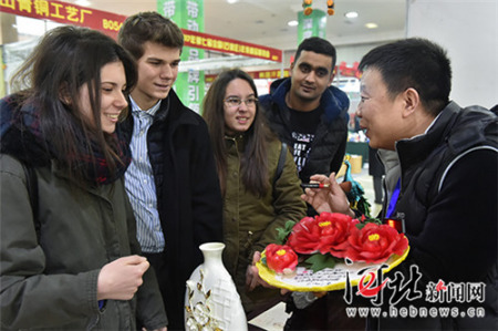 一位陶瓷商正向幾名來自石家莊四十二中的外國留學生介紹中國傳統(tǒng)節(jié)日飾品牡丹瓷。