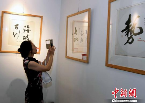 一名女性觀眾用手機拍攝參展書法作品?！∮浾邉⒖筛?攝