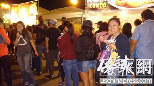 圣蓋博教會路餃子攤亭一個挨一個，每個攤亭前都大排長龍，圣蓋博居民鄧曉玲女士(右二)一邊吃餃子一邊排隊。(僑報記者高睿攝)