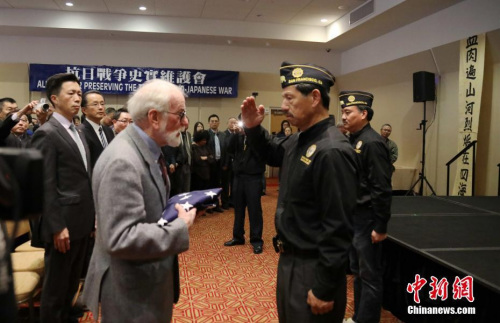 12月10日下午，美國舊金山中華文化中心，中英文口號聲不斷響起，由南京大屠殺索賠聯(lián)盟、舊金山灣區(qū)中國統(tǒng)一促進(jìn)會、舊金山抗日史實維護(hù)會和慰安婦正義聯(lián)盟聯(lián)合主辦的“南京祭”紀(jì)念活動進(jìn)入第21年。圖為中國駐舊金山代總領(lǐng)事查立友（左一）、南京大屠殺索賠聯(lián)盟前主席羅杰斯·斯科特（左二）接受美國退伍軍人協(xié)會華系支會轉(zhuǎn)交美國國旗。<a target='_blank' >中新社</a>記者 劉丹 攝