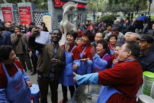 圖7：2015年農(nóng)歷二月初二，當(dāng)日來(lái)紅日亭吃芥菜飯的路人很多，溫州醫(yī)學(xué)院留學(xué)生艾鵬達(dá)聞?dòng)嵑髞?lái)紅日亭當(dāng)義工。在場(chǎng)的紅日亭老人們紛紛與艾鵬達(dá)開(kāi)心留影。
