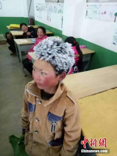 2018年1月9日，云南昭通一名頭頂風霜上學的孩子照片在網(wǎng)上引起廣泛關(guān)注。照片中的孩子站在教室里，頭發(fā)和眉毛已經(jīng)被風霜粘成雪白，臉蛋通紅，穿著并不厚實的衣服，身后的同學看著他的“冰花”造型大笑。文字來源：人民日報 圖片來源：視覺中國