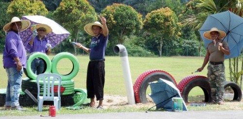 大家戴著草帽、撐著傘，在烈日下美化校園。（馬來西亞《星洲日報》）
