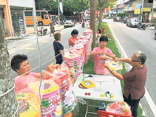 村民分工合作將透明的塑料袋倒套著紙制的燈籠，避免燈籠被雨淋濕或被曝曬損壞。（馬來西亞《中國報》/村民提供照片）