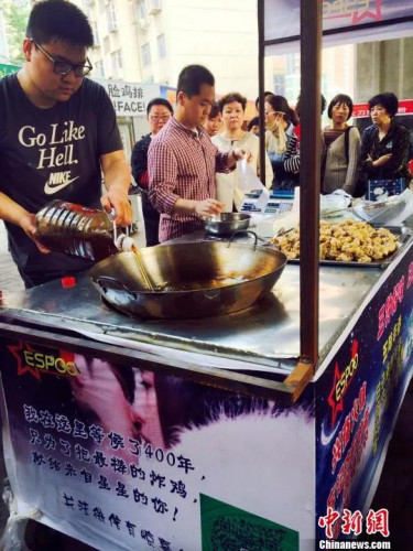 郭方正(左)正在往鍋里倒炸雞用的油，攤位邊等待的顧客已排起長(zhǎng)隊(duì)?！〔苠P 攝