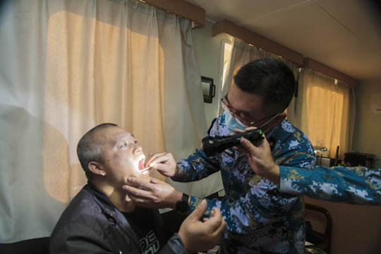 中國僑網(wǎng)兩位軍醫(yī)檢查患者咽部情況。
